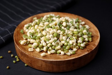 Photo of Wooden plate with sprouted green mung beans on black background, closeup