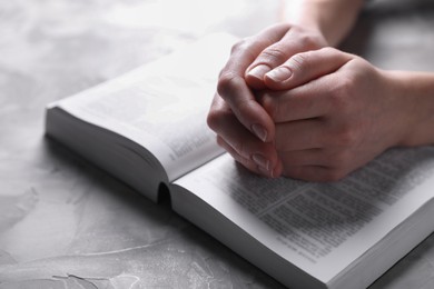 Religion. Christian woman praying over Bible at gray textured table, closeup