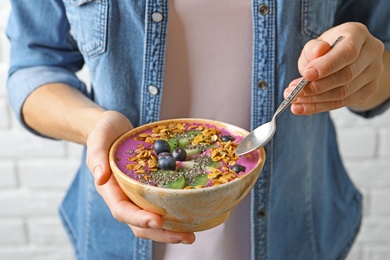 Photo of Woman eating acai smoothie with granola and berries, closeup