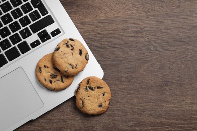 Photo of Chocolate chip cookies and laptop on wooden table, flat lay. Space for text