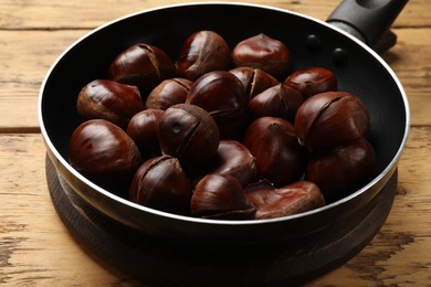 Photo of Fresh edible sweet chestnuts in frying pan on wooden table, closeup