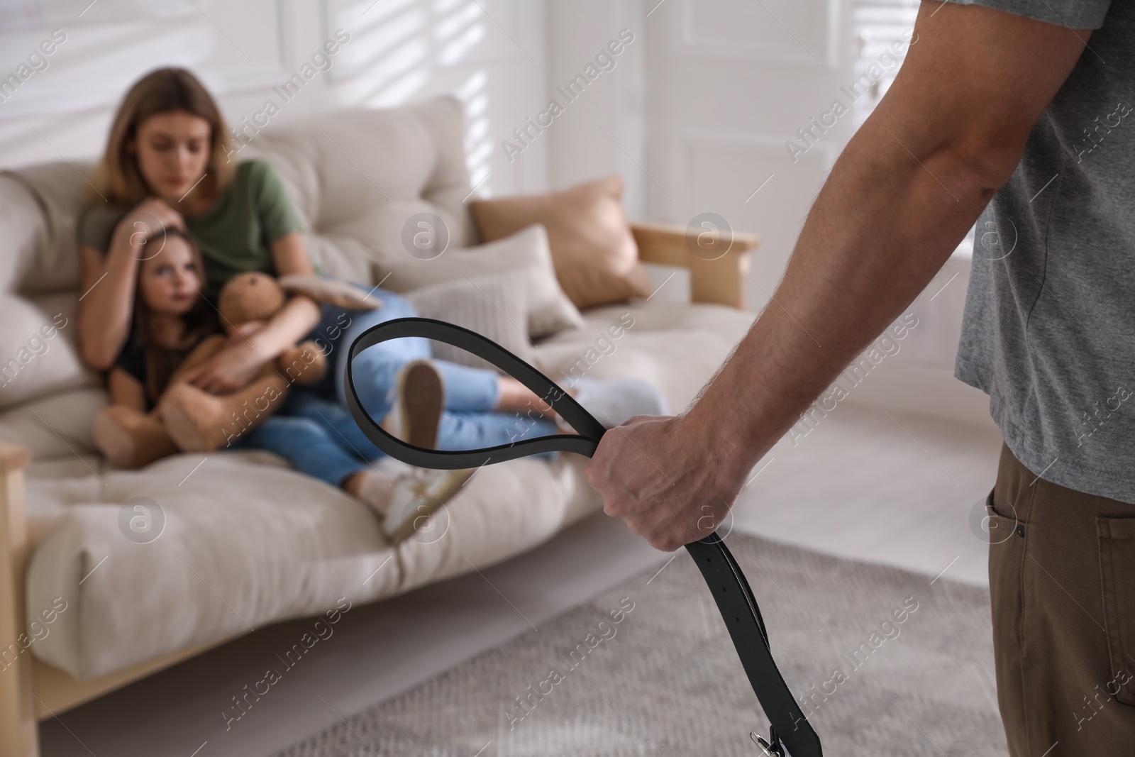 Photo of Man threatening his wife and daughter with belt at home, closeup. Domestic violence