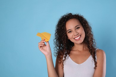 Photo of Beautiful African-American woman playing with paper plane on light blue background. Space for text