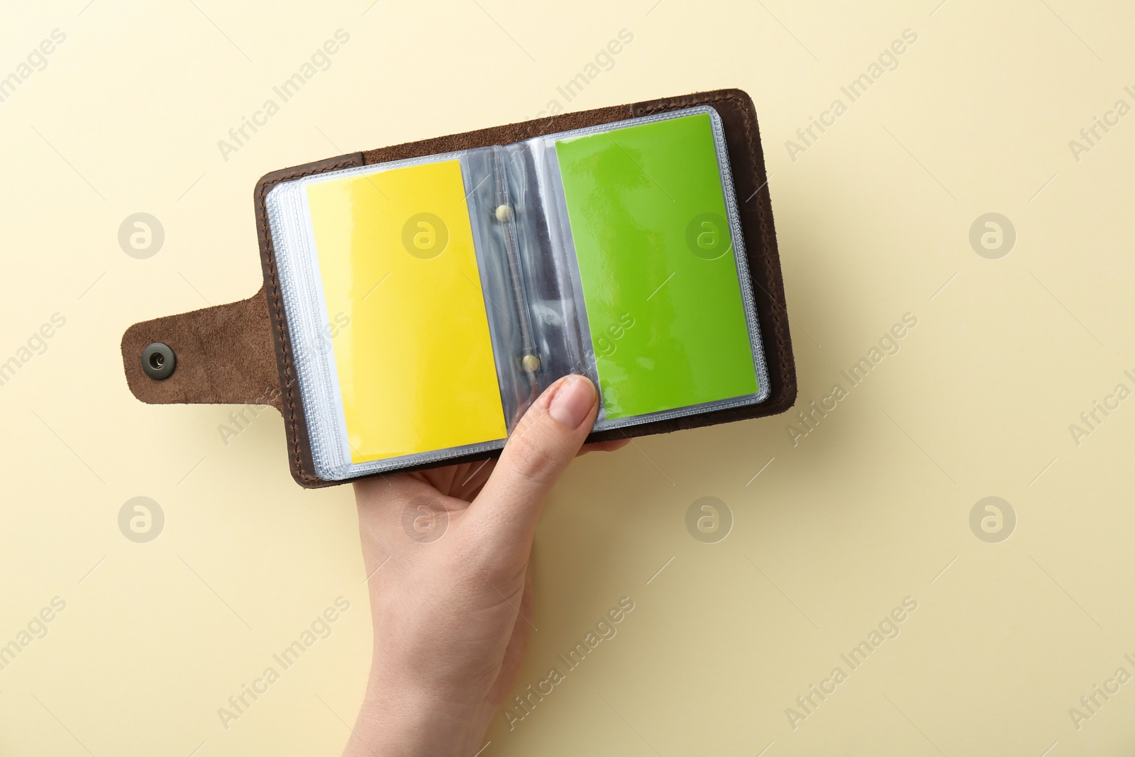 Photo of Woman holding business card holder with colorful cards on light yellow background, top view