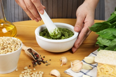 Photo of Woman mixing pesto sauce with pestle in mortar at table, closeup