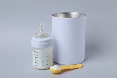 Photo of Blank can of powdered infant formula with scoop and feeding bottle on light grey background. Baby milk