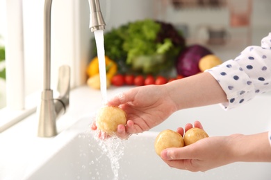 Photo of Woman washing fresh potatoes in kitchen sink, closeup