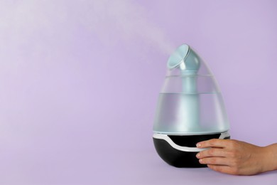Woman using modern air humidifier on violet background, closeup. Space for text
