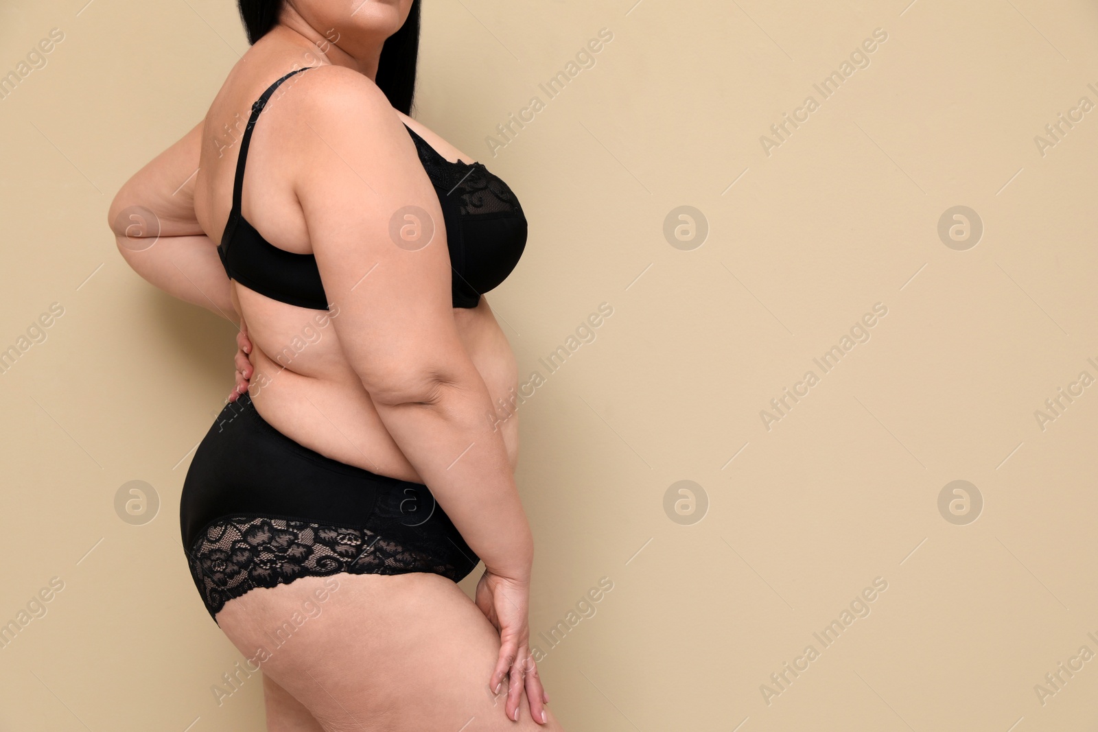 Photo of Beautiful overweight woman in black underwear on beige background, closeup with space for text. Plus-size model