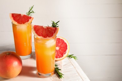 Photo of Tasty grapefruit drink with ice in glasses, rosemary and fresh fruits on light wooden table. Space for text
