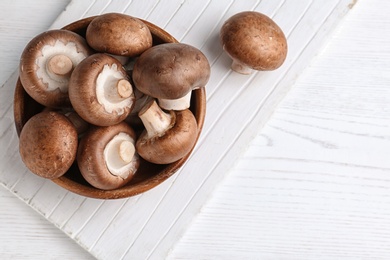 Bowl with fresh champignon mushrooms on wooden table, top view. Space for text