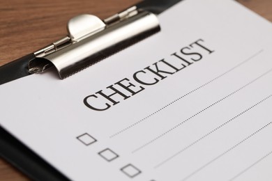 Clipboard with inscription Checklist on wooden table, closeup