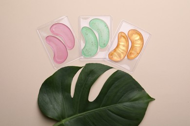 Photo of Under eye patches and tropical leaf on beige background, flat lay. Cosmetic product