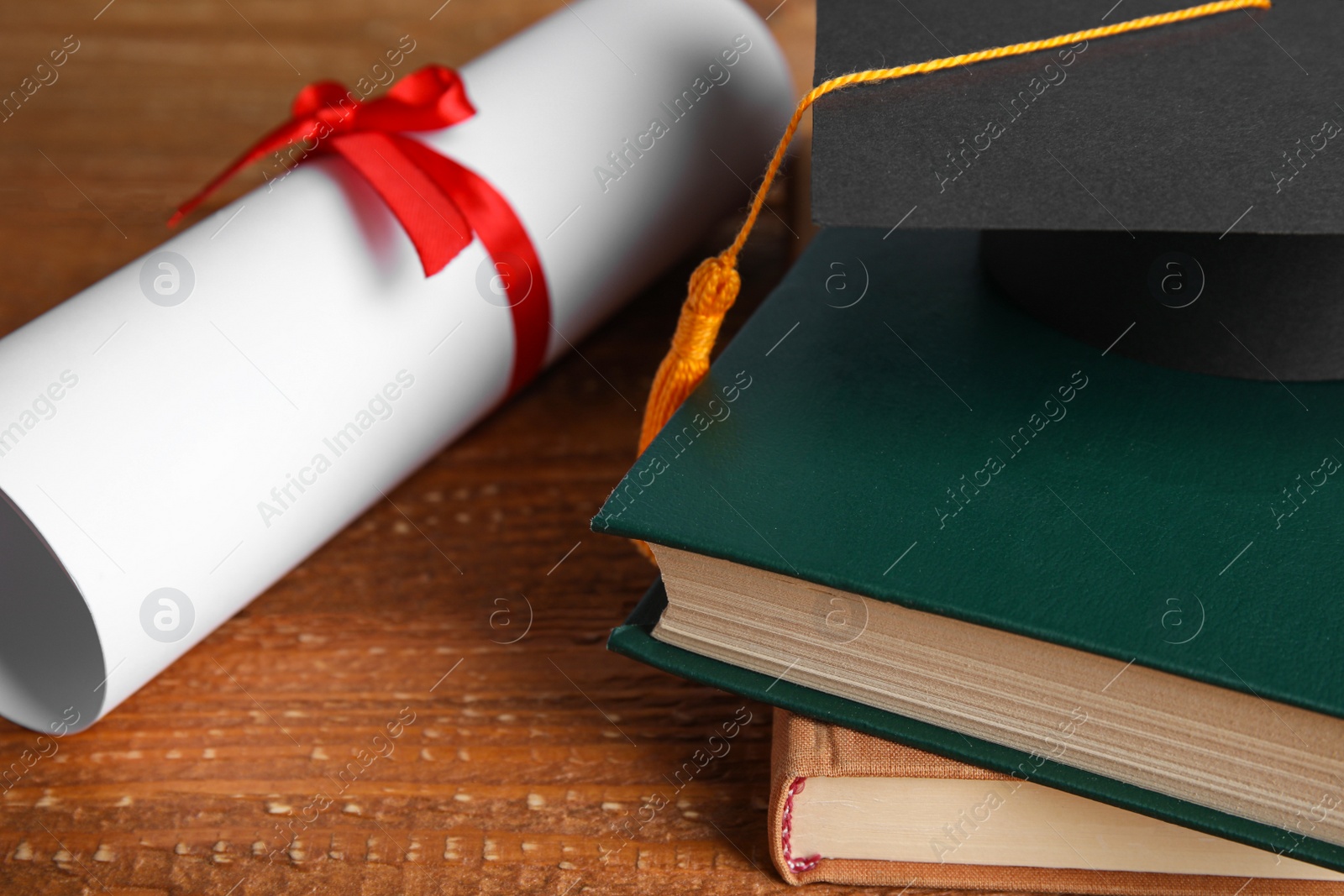 Photo of Graduation hat, books and student's diploma on wooden table, closeup