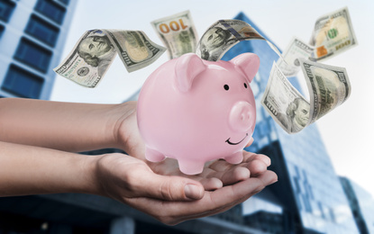 Image of Woman holding piggy bank and American dollars falling outdoors, closeup 