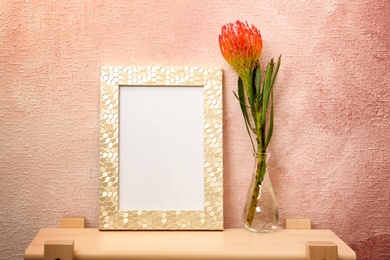 Photo of Blank frame and vase with flower on table near color wall. Mock up for design