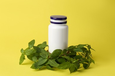 Photo of Medicine bottle near green leaves on yellow background