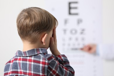 Ophthalmologist testing little boy's vision in clinic, back view