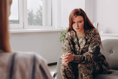 Sad female military officer sitting on sofa in psychologist office