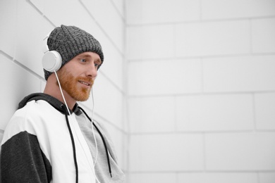 Young man listening to music with headphones near light wall. Space for text