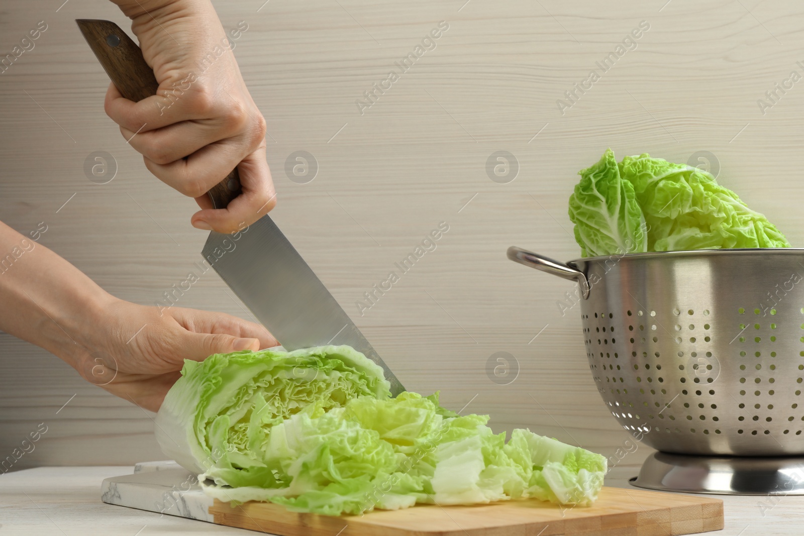 Photo of Woman cutting Chinese cabbage at white wooden kitchen table, closeup