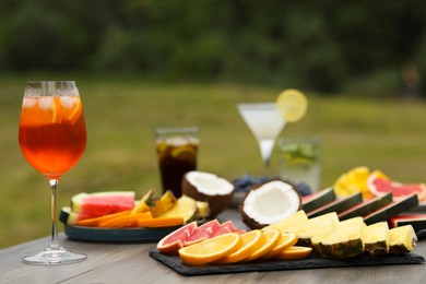Photo of Glasses of cocktails and fruits on wooden table outdoors, closeup