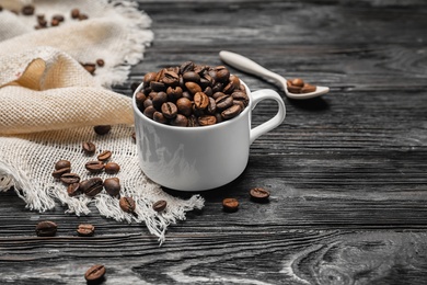 Cup with roasted coffee beans on wooden background