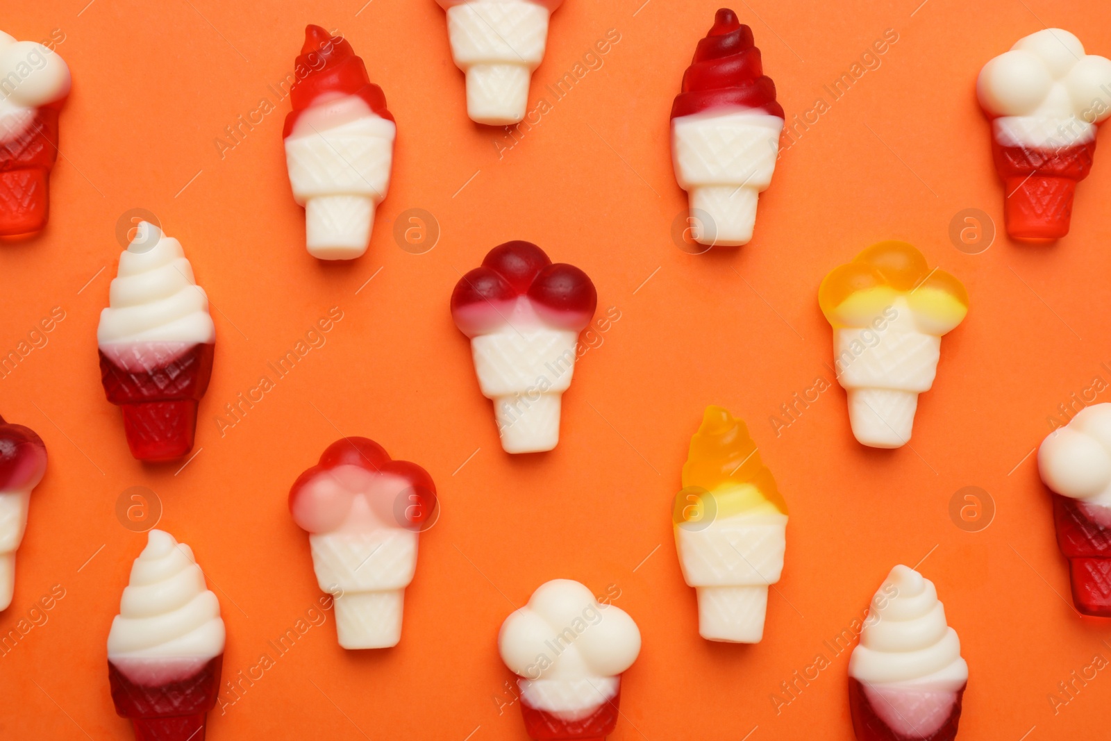 Photo of Delicious gummy ice cream cones candies on orange background, flat lay