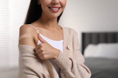 Photo of Woman with sticking plaster on arm after vaccination showing thumbs up in bedroom, closeup