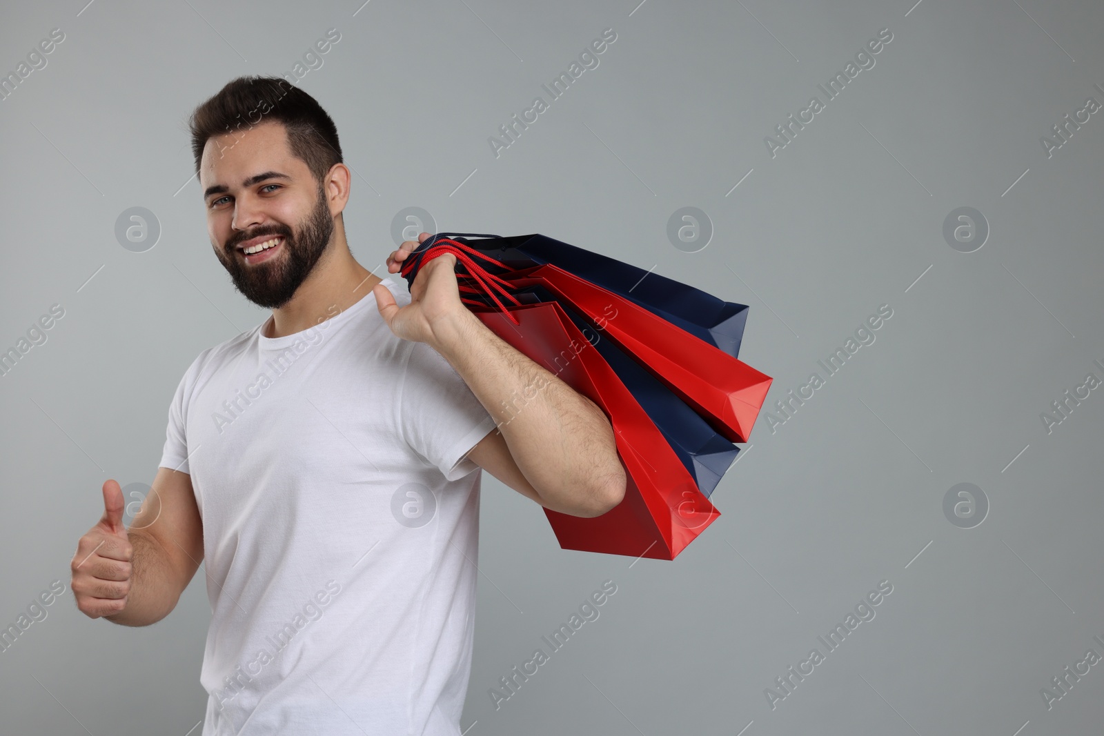 Photo of Happy man with many paper shopping bags showing thumb up on grey background. Space for text