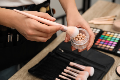 Professional makeup artist with brush and blusher at wooden table indoors, closeup