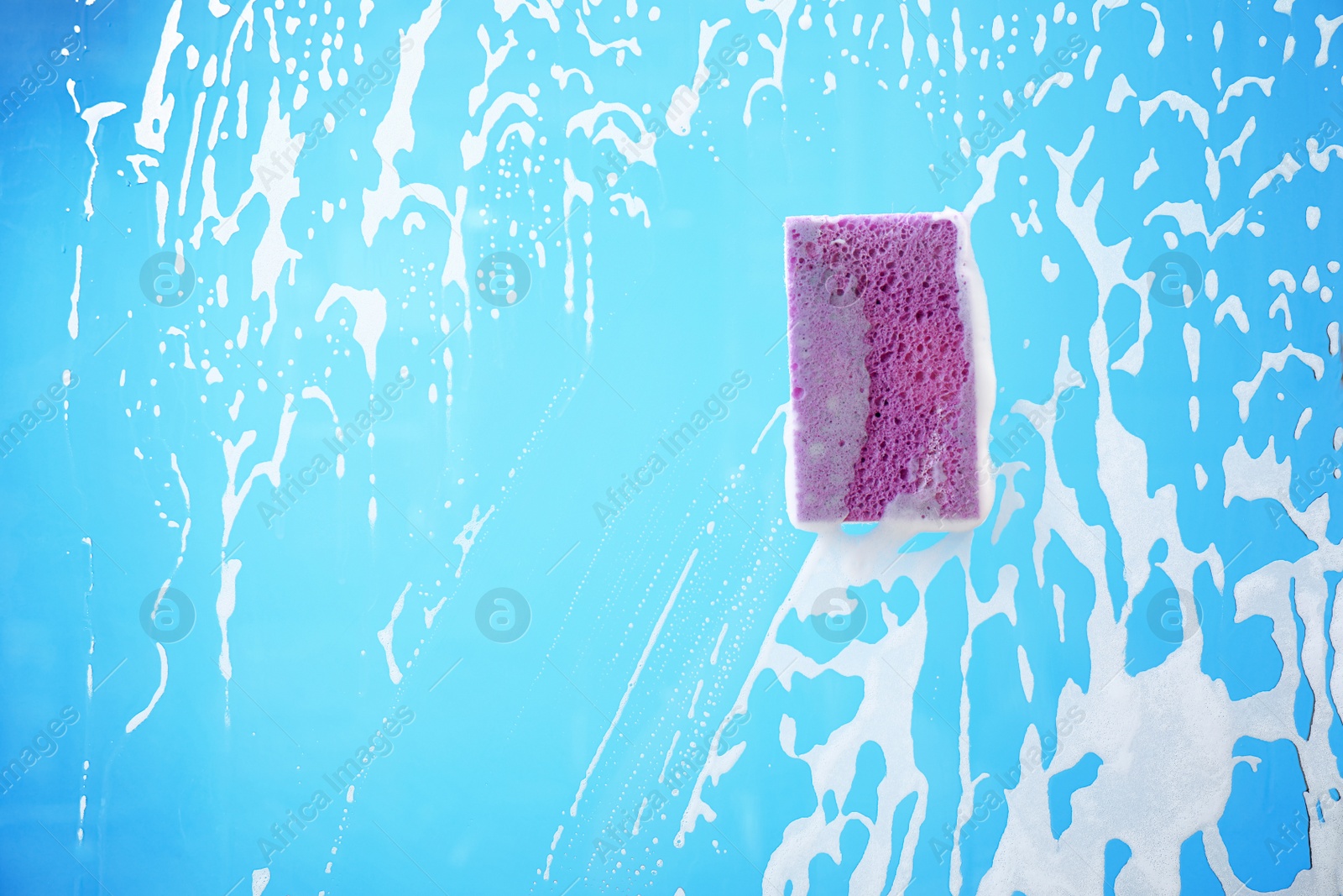 Photo of Sponge on glass covered with suds against color background