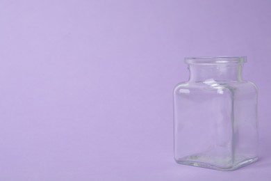 Photo of Open empty glass jar on lilac background, space for text