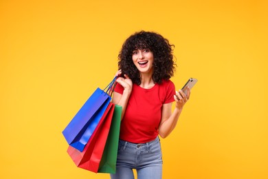 Photo of Happy young woman with shopping bags and modern smartphone on yellow background