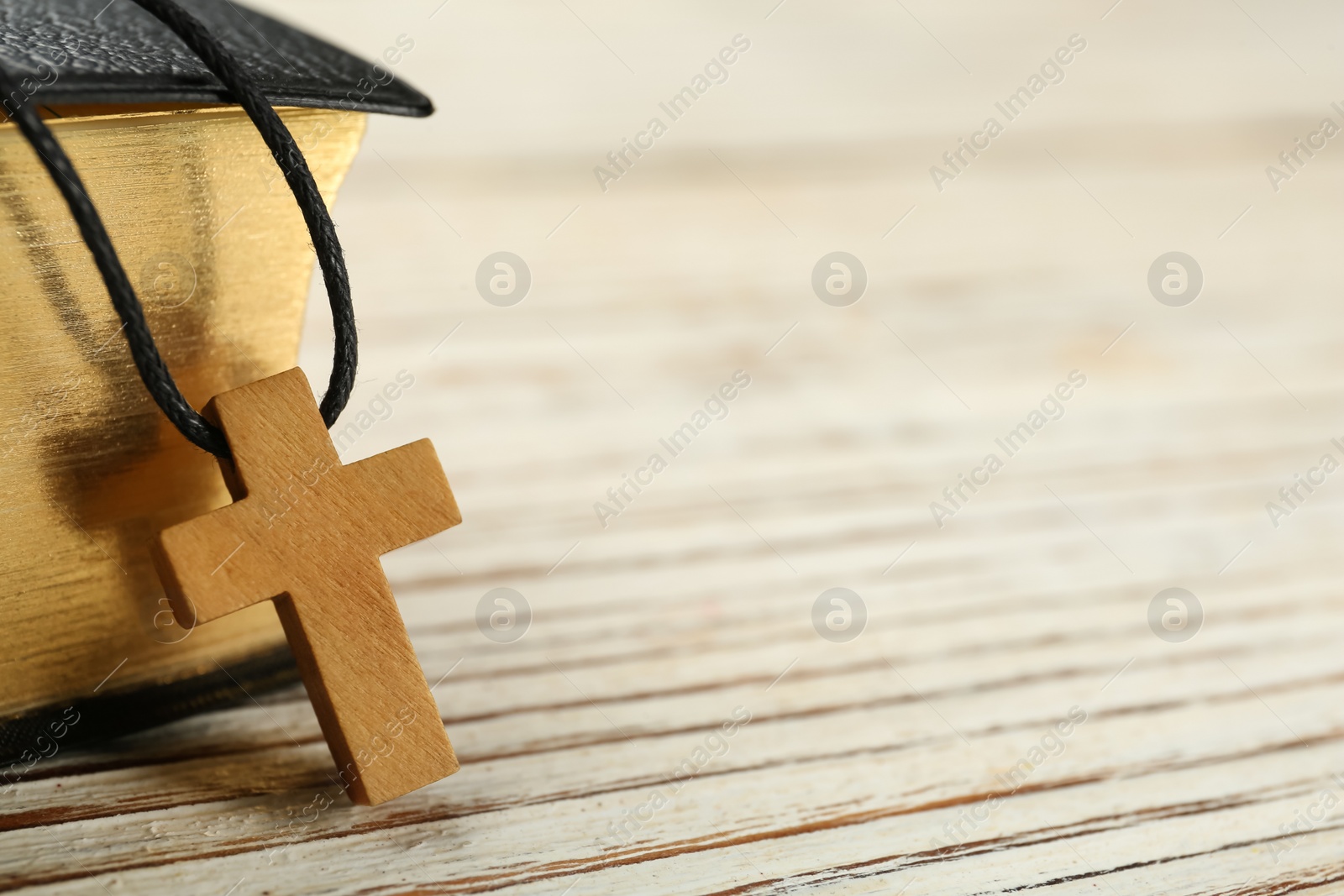 Photo of Christian cross and Bible on white wooden table, closeup. Space for text