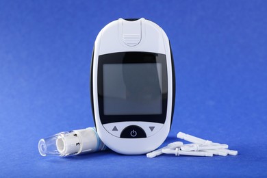 Photo of Digital glucometer, lancets and pen on blue background. Diabetes control