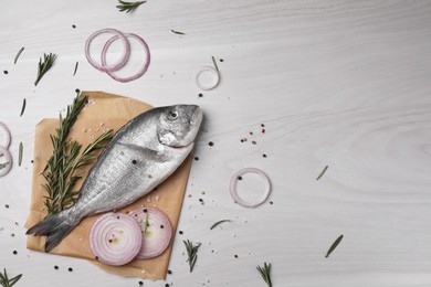 Photo of Raw dorado fish, spices and onion on white wooden table, flat lay