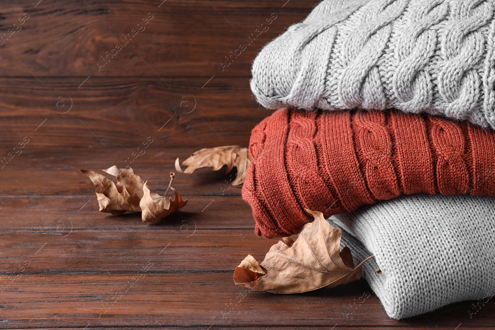 Image of Stack of folded warm sweaters and dry leaves on wooden background