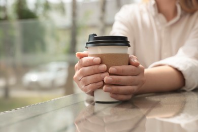 Photo of Woman holding paper takeaway cup at glass table outdoors, closeup. Coffee to go
