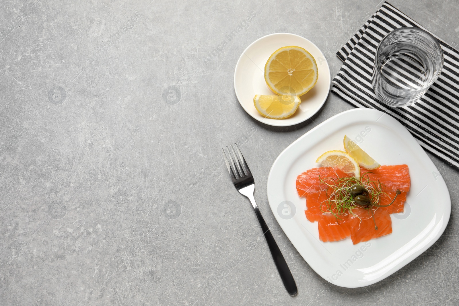 Photo of Salmon carpaccio with capers, microgreens and lemon served on grey table, flat lay. Space for text