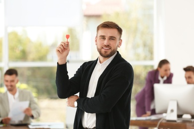 Happy young businessman with dart in office