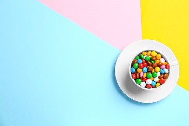 Cup with delicious bright glazed candies on color background, top view. Space for text