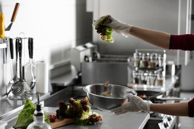 Photo of Female chef cooking tasty salad in restaurant kitchen, closeup