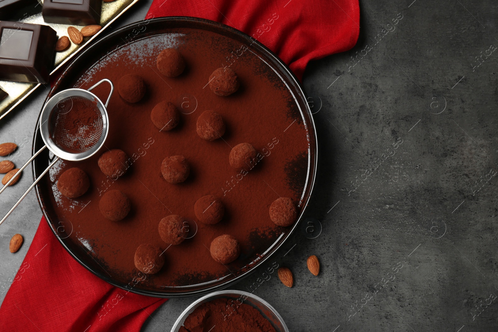 Photo of Delicious chocolate candies powdered with cocoa, sieve and ingredients on grey table, flat lay. Space for text