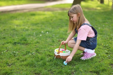 Photo of Easter celebration. Cute little girl with bunny ears hunting eggs outdoors, space for text
