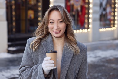Photo of Portrait of smiling woman with paper cup of coffee on city street in winter