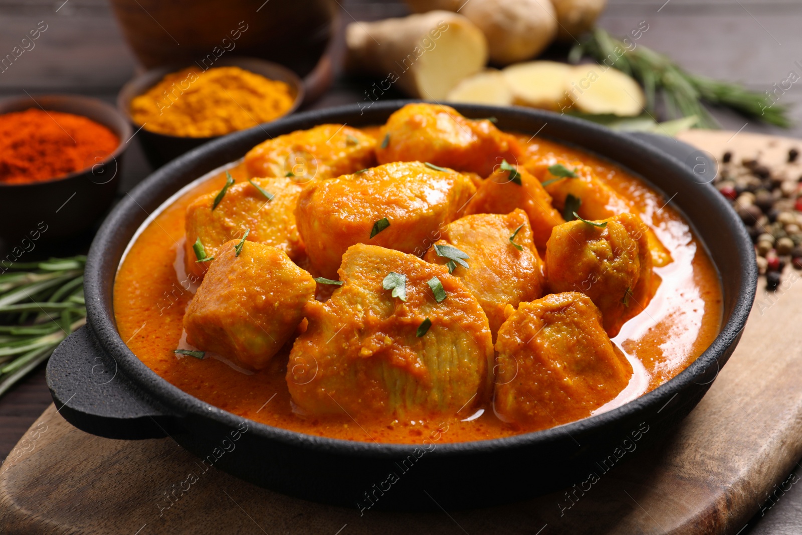 Photo of Delicious chicken curry in pan on wooden board, closeup