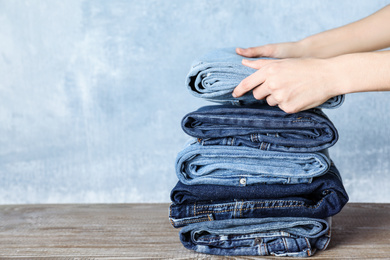 Woman folding stylish jeans on wooden table, closeup. Space for text