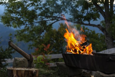 Photo of Metal brazier with burning firewood on backyard in mountains
