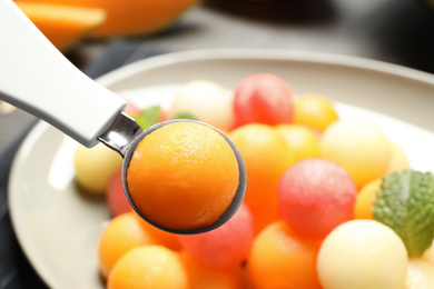 Photo of Scoop with melon ball near plate of fruit salad, closeup